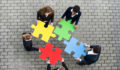 Image of business people holding puzzle pieces, trying to figure out where they fit.