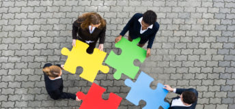 Image of business people holding puzzle pieces, trying to figure out where they fit.