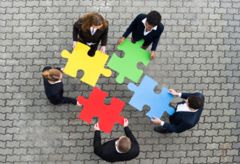 Image of business people holding puzzle pieces, trying to figure out where they fit.