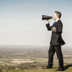 Hold your heads high, expert urges industry Picture of a businessman with loudhailer megaphone on hill.