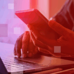 A person is reading their phone while sitting in front of a laptop