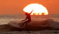 Image of a surfer riding a wave during sunset.